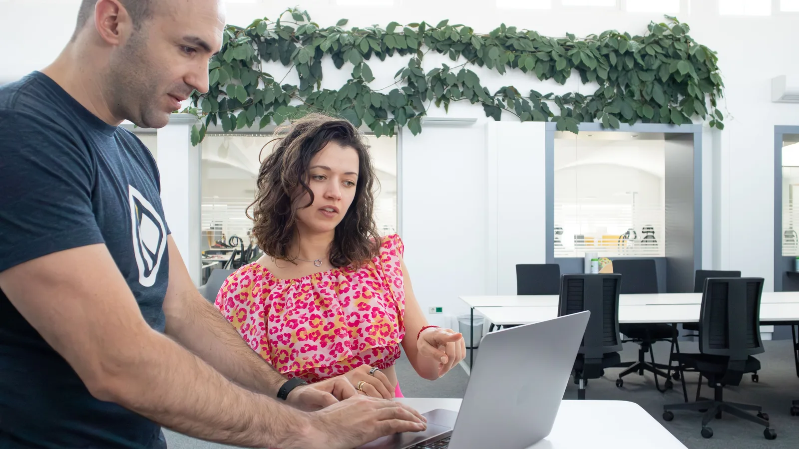 Two colleagues reviewing work together on a laptop in a bright office.